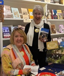 Image of two older women, Judilee Butler and GaGa Gabardi, coauthors, one is a member of the Space Coast Writers Guild, standing in front of a white bookshelf